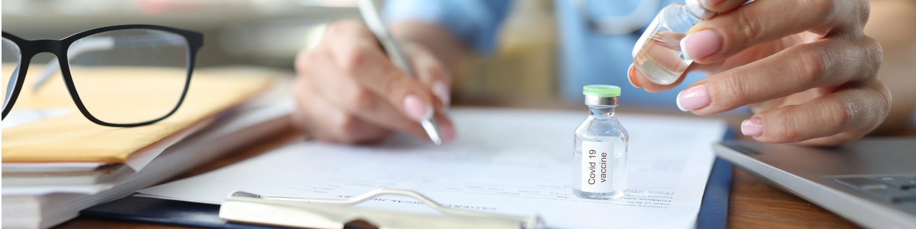 doctor-writing-in-document-on-board-at-table-and-holding-bottle-with 1900 x 500