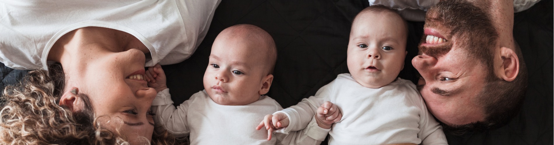 happy-parents-lying-in-bed-with-their-twin-baby-boys-and-smiling-1900x500