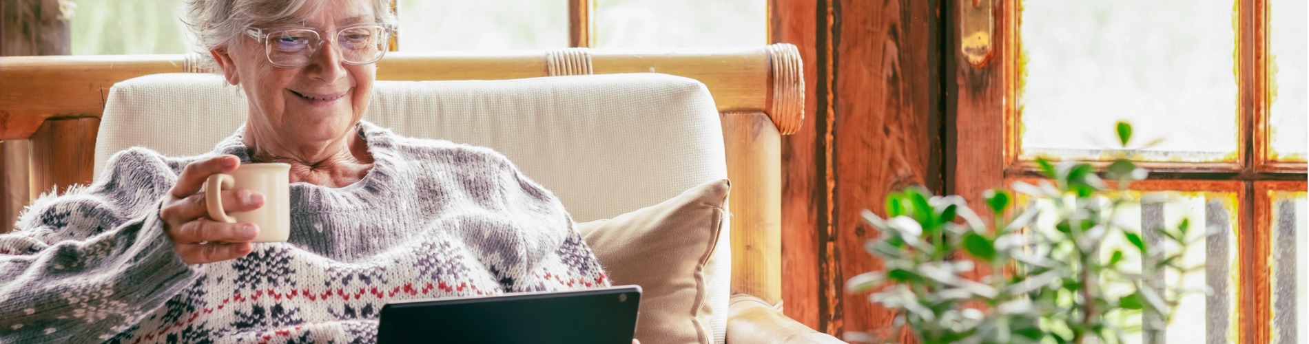 old-senior-woman-sitting-at-home-on-armchair-using-digital-tablet-wearing-a-warm-sweater-and.1900x500jpg
