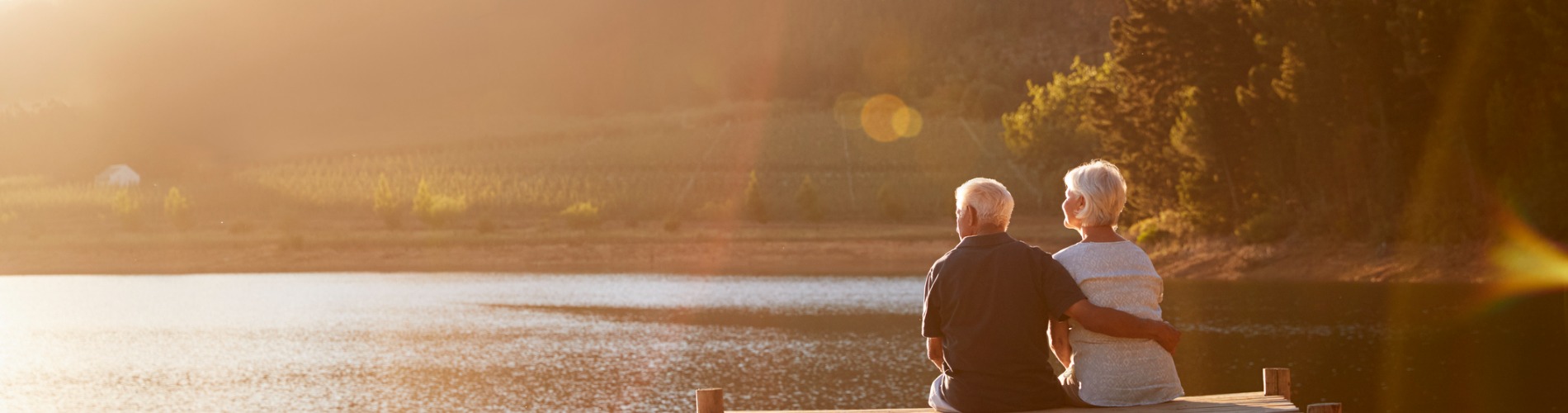 romantic-senior-couple-sitting-on-wooden-jetty-by-lake-1900x500